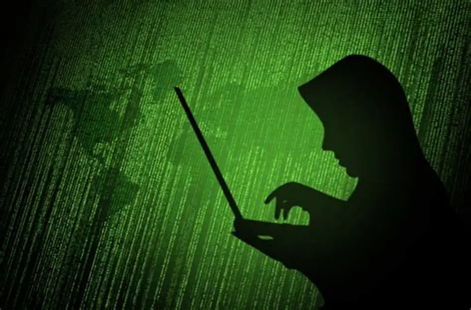 Dark web threats represented by hooded hacker silhouette typing on laptop with green code background